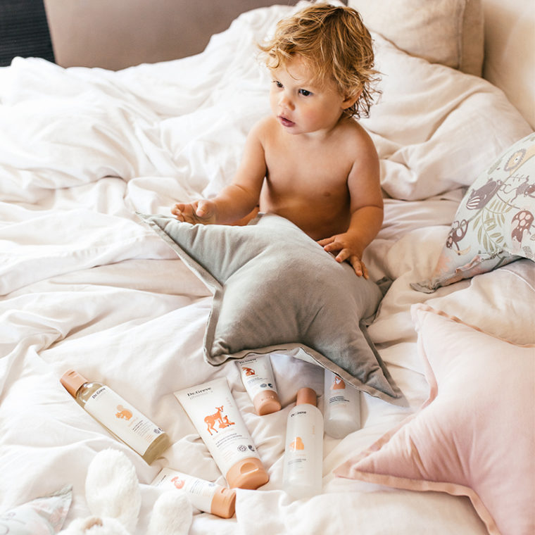 Et barn sitter i sengen med Dr. Greve pharma produktene foran seg