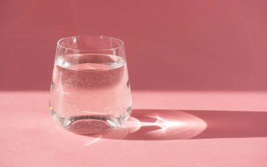 Vannglass foran rosa bakgrunn. Hold deg hydrert for å redde tørre lepper.