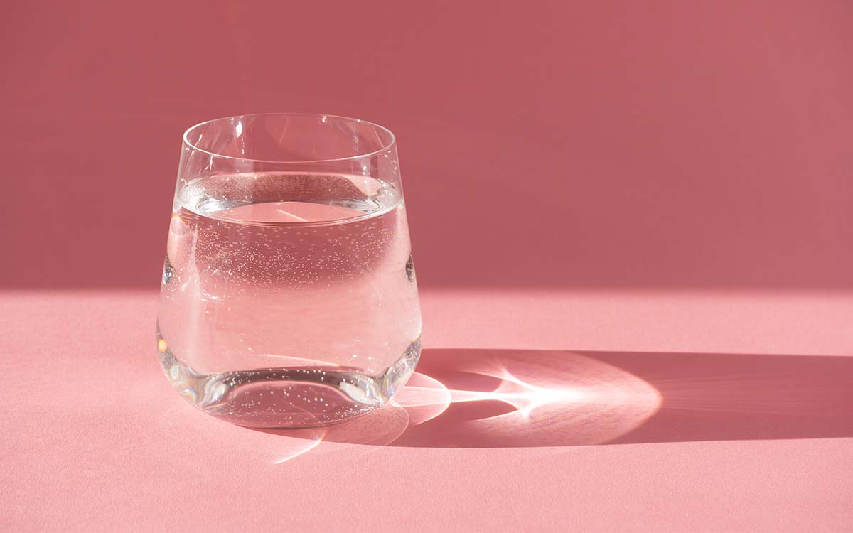 Vannglass foran rosa bakgrunn. Hold deg hydrert for å redde tørre lepper.